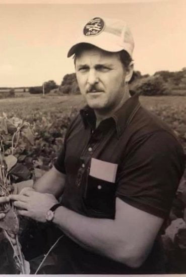 Pop wearing a camo cap and red plaid shirt by the water.