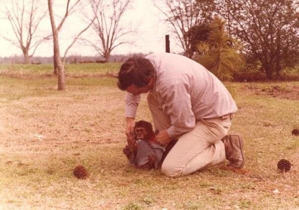 Pop kneeling in the yard, holding Otis the stump-tailed macaque.