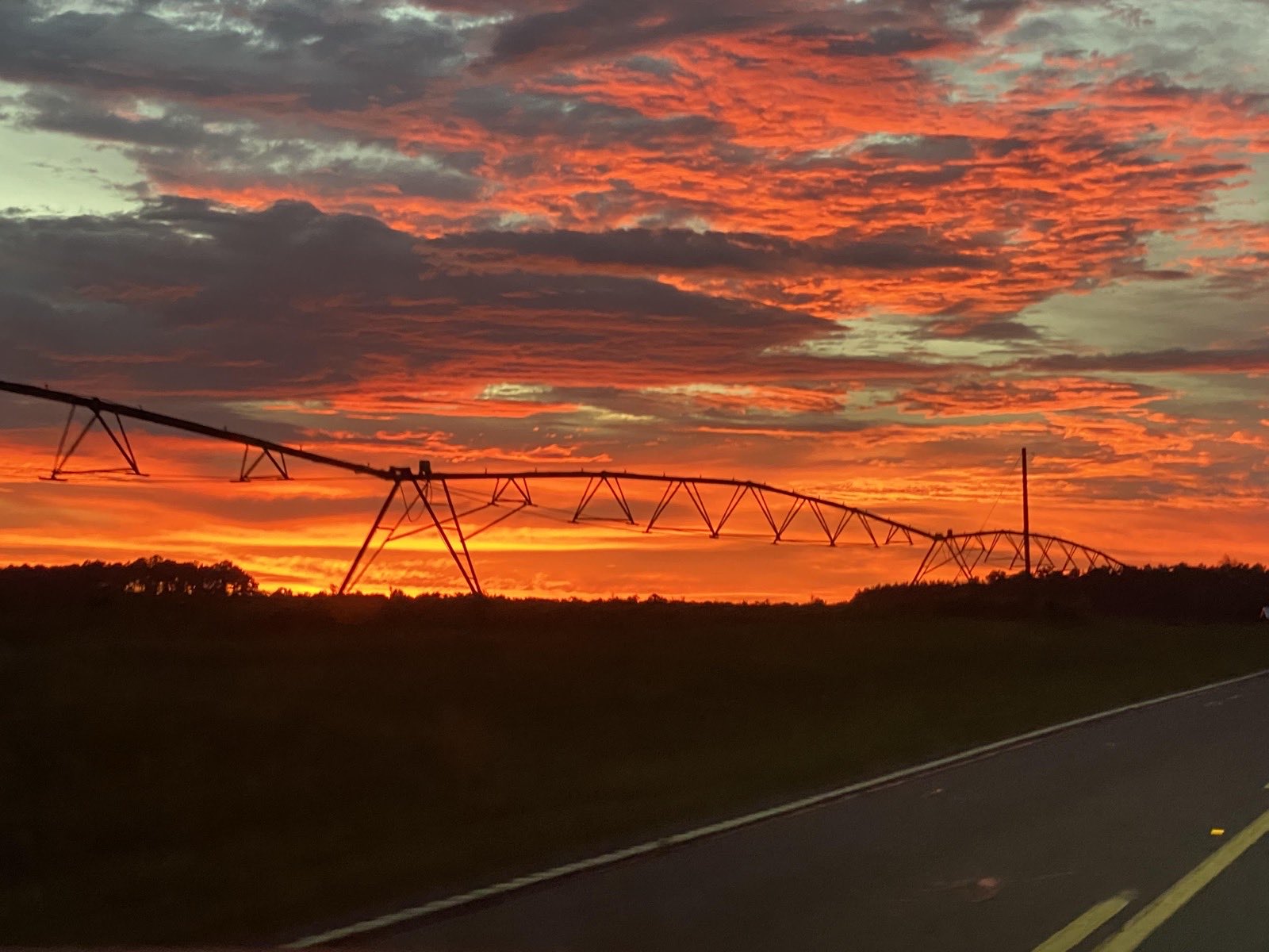 A fiery orange sunset over farmland, with an irrigation pivot silhouetted against the sky.